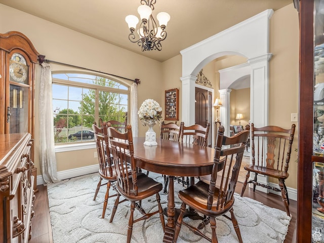 dining room featuring ornate columns, arched walkways, baseboards, a chandelier, and wood finished floors
