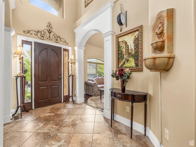 entrance foyer featuring ornate columns, arched walkways, baseboards, a towering ceiling, and stone tile floors