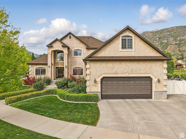 french country inspired facade with stucco siding, concrete driveway, a mountain view, and a gate