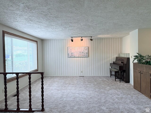 living area featuring carpet flooring, a textured ceiling, baseboards, and track lighting