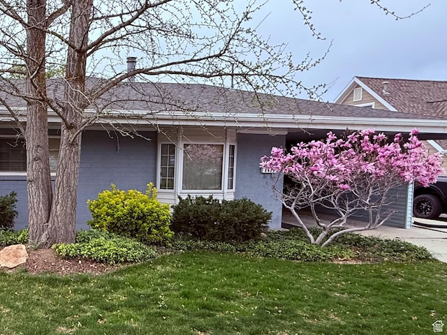 view of side of property with brick siding, a yard, and roof with shingles