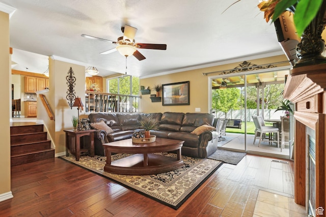 living room with ceiling fan, crown molding, stairway, hardwood / wood-style floors, and a fireplace