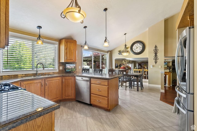 kitchen with appliances with stainless steel finishes, a sink, plenty of natural light, brown cabinets, and vaulted ceiling