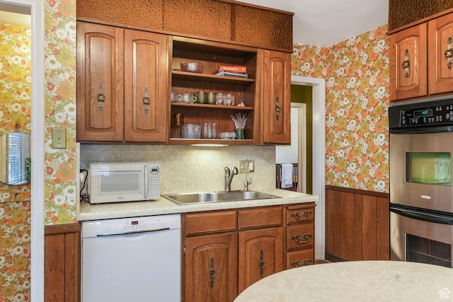 kitchen featuring white appliances, wallpapered walls, a sink, a wainscoted wall, and light countertops