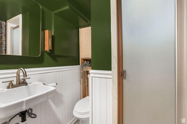 bathroom with a wainscoted wall, toilet, and a sink