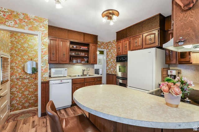kitchen with white appliances, wallpapered walls, a sink, open shelves, and light wood-style floors