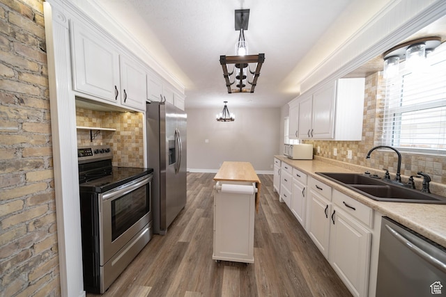 kitchen with stainless steel appliances, a sink, a chandelier, a center island, and white cabinetry