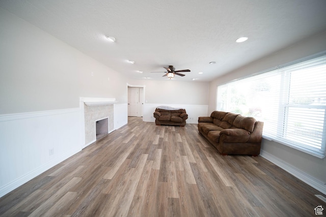 living room featuring wood finished floors, ceiling fan, a fireplace, baseboards, and recessed lighting