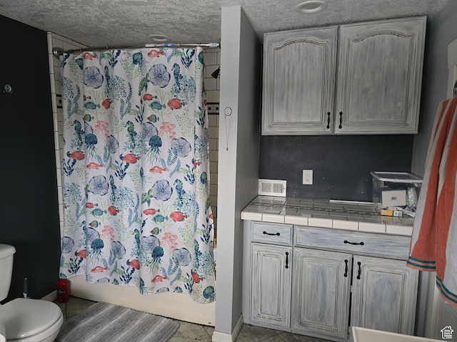 bathroom featuring shower / bath combo, toilet, a textured ceiling, baseboards, and tile patterned floors