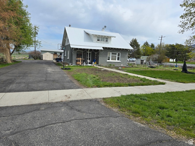 view of front of property featuring a front yard, an outdoor structure, covered porch, metal roof, and stucco siding