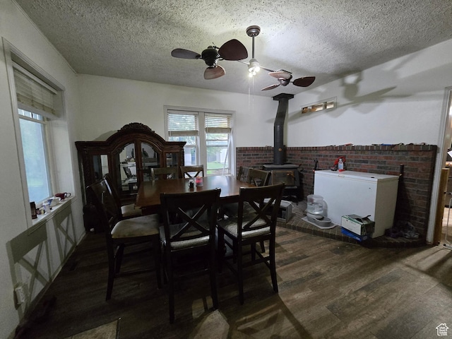 dining room featuring ceiling fan, a wood stove, a textured ceiling, wood finished floors, and healthy amount of natural light