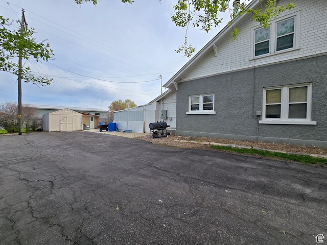 view of side of property with a storage shed, an outdoor structure, stucco siding, and asphalt driveway