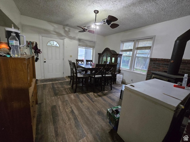dining area featuring a ceiling fan, dark wood-type flooring, a wood stove, and a textured ceiling