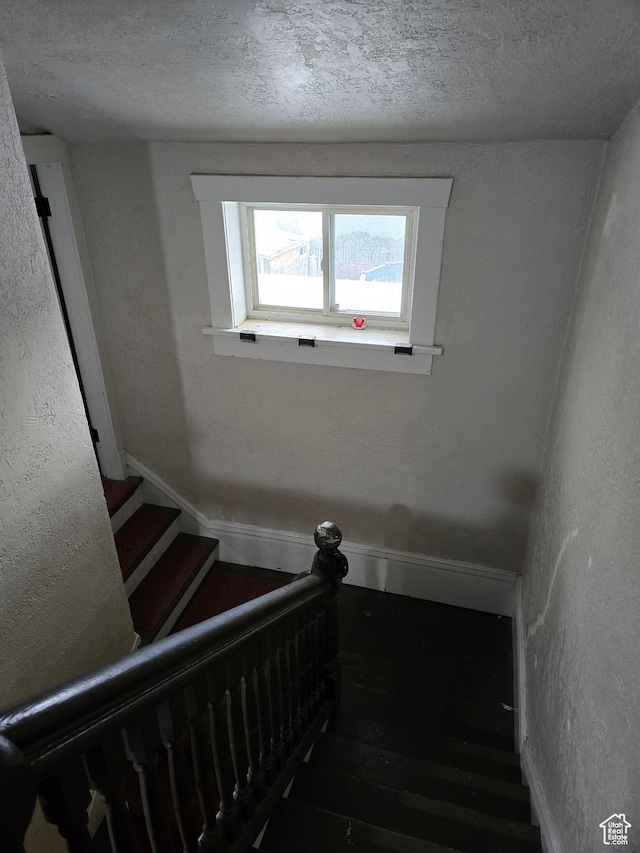 staircase with a textured ceiling and wood finished floors