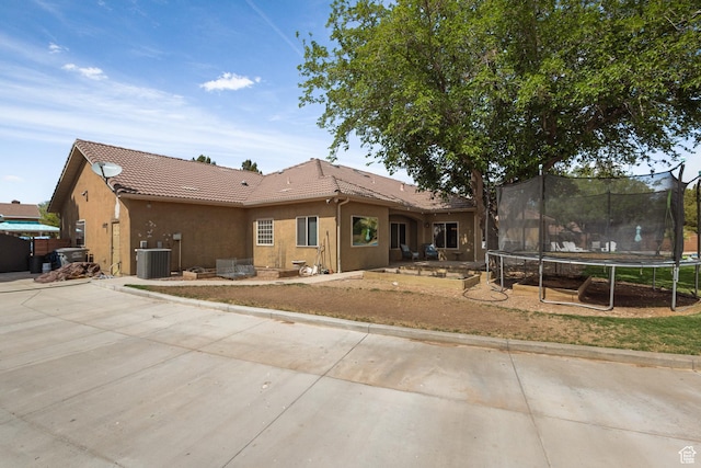 rear view of house with a trampoline, a tiled roof, and stucco siding