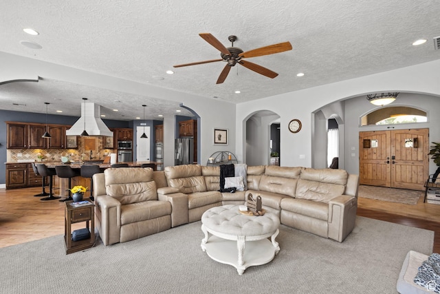 living room with arched walkways, a ceiling fan, a textured ceiling, recessed lighting, and light wood-style floors