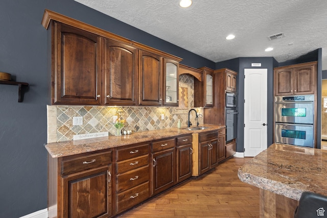 kitchen with a sink, appliances with stainless steel finishes, wood-type flooring, light stone countertops, and decorative backsplash
