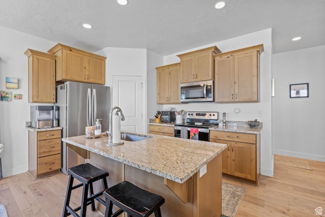 kitchen with stainless steel appliances, a sink, baseboards, a kitchen island with sink, and light stone countertops