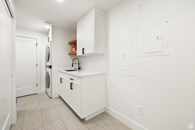 clothes washing area with stacked washer / drying machine, a sink, and baseboards