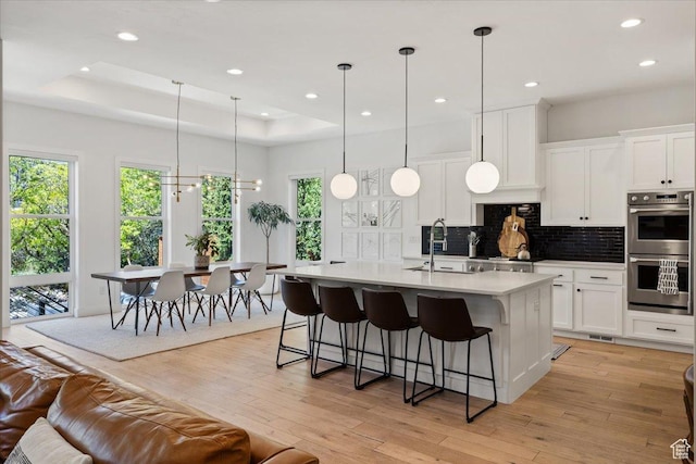 kitchen featuring double oven, a sink, backsplash, a tray ceiling, and light wood finished floors