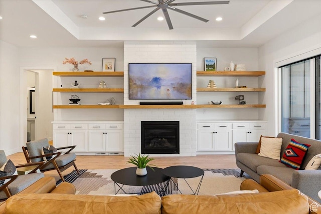 living area featuring a fireplace, ceiling fan, light wood-style floors, a tray ceiling, and recessed lighting
