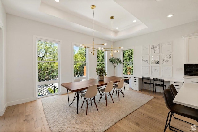 dining space with a raised ceiling, light wood-type flooring, a chandelier, recessed lighting, and baseboards