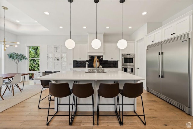 kitchen with appliances with stainless steel finishes, backsplash, light countertops, white cabinetry, and light wood-style flooring