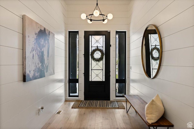 foyer entrance with hardwood / wood-style floors, wooden walls, and a chandelier