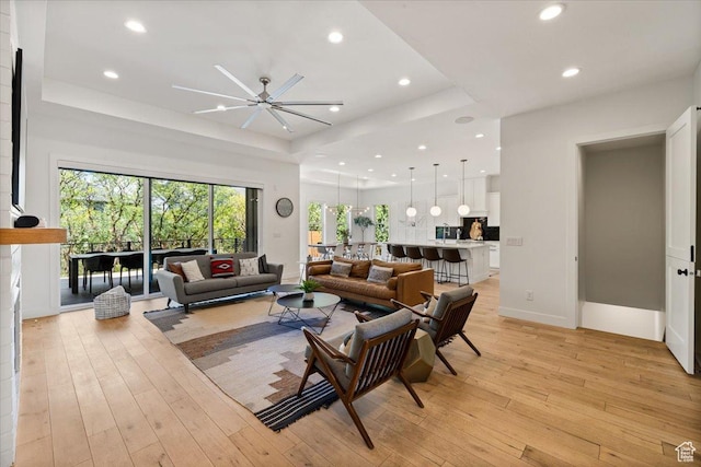 living area featuring a raised ceiling, recessed lighting, ceiling fan, light wood-style flooring, and baseboards