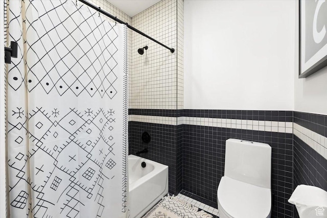 bathroom featuring tile walls, shower / bath combo with shower curtain, toilet, tile patterned flooring, and wainscoting