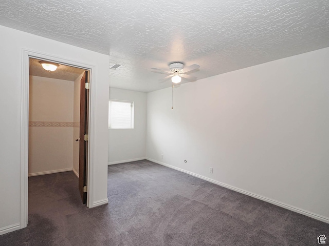 unfurnished bedroom with dark colored carpet, a textured ceiling, a ceiling fan, baseboards, and a walk in closet