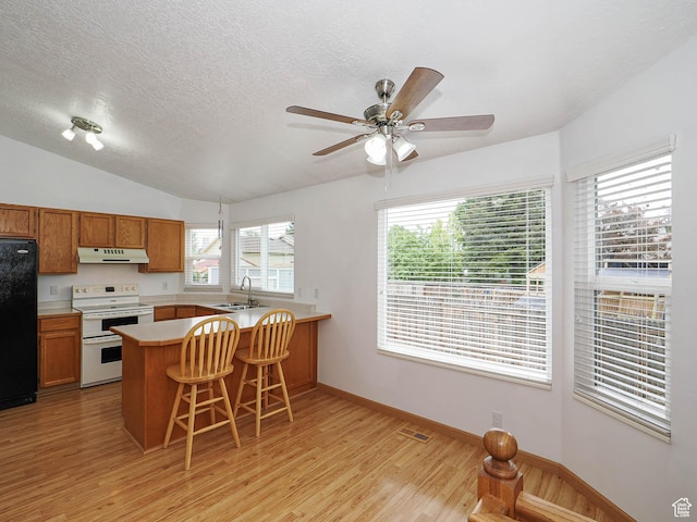 kitchen with double oven range, under cabinet range hood, fridge, light wood-style flooring, and a peninsula
