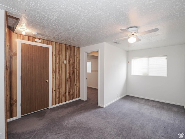carpeted spare room featuring a textured ceiling, a ceiling fan, wooden walls, and baseboards