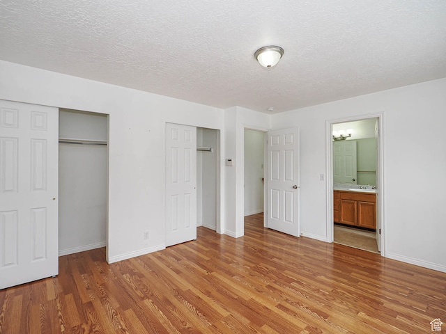 unfurnished bedroom featuring multiple closets, light wood-style floors, a textured ceiling, baseboards, and a sink