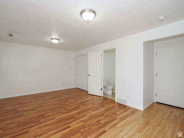 empty room with light wood-style floors, a textured ceiling, baseboards, and a smoke detector