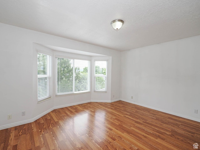 unfurnished room with wood finished floors, healthy amount of natural light, and baseboards