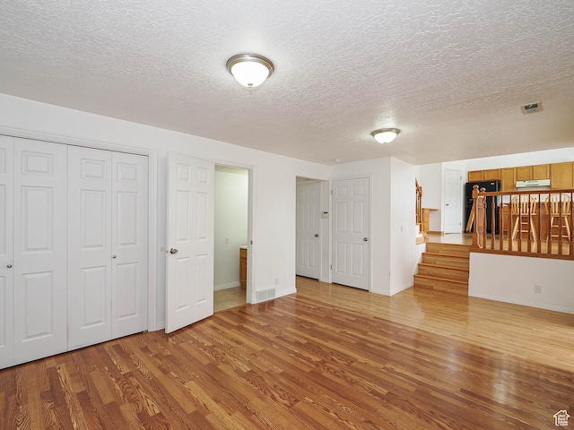 unfurnished living room featuring wood finished floors, a textured ceiling, baseboards, and stairway