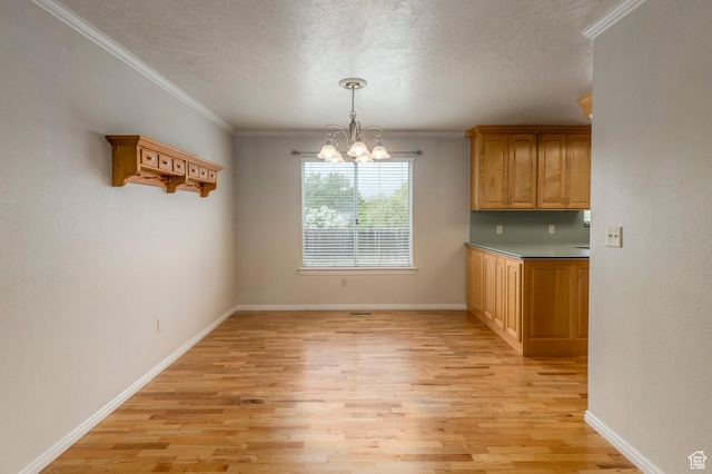 unfurnished dining area with a chandelier, light wood-style floors, a textured ceiling, ornamental molding, and baseboards