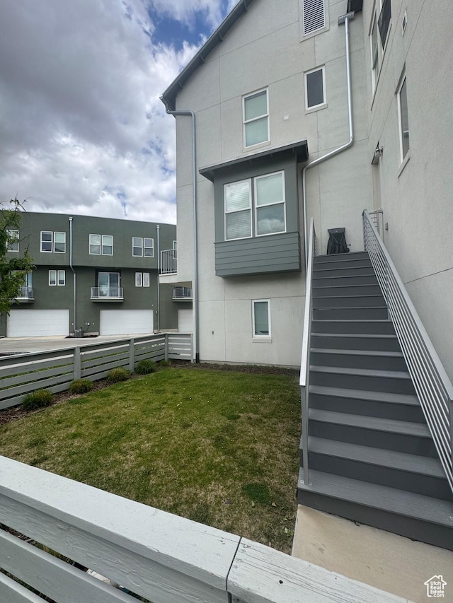 rear view of house with fence, a wall mounted AC, stucco siding, and stairs