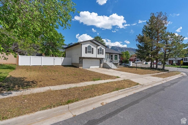 tri-level home with concrete driveway, fence, an attached garage, and a mountain view