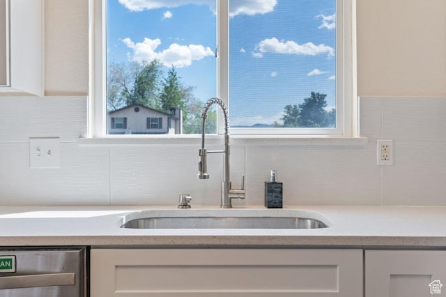 kitchen view of a sink, dishwasher, white cabinets, and decorative backsplash