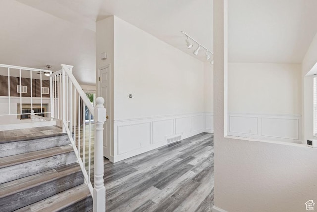 staircase featuring wood finished floors, a wainscoted wall, and a decorative wall