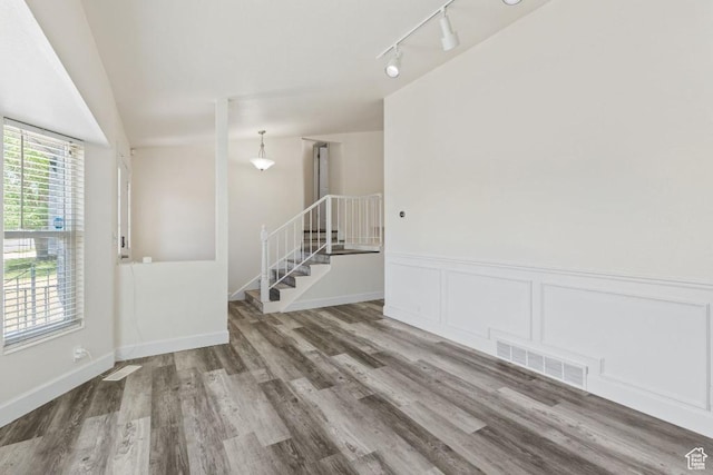 unfurnished room featuring wood finished floors, rail lighting, and wainscoting