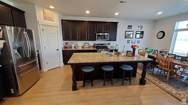 kitchen featuring appliances with stainless steel finishes, a kitchen bar, light stone counters, light wood finished floors, and recessed lighting