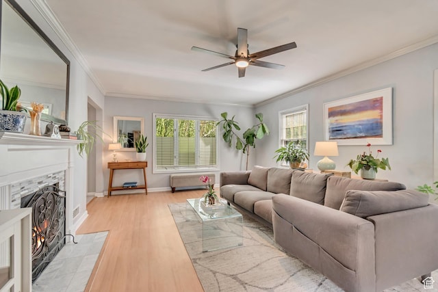 living area with a ceiling fan, a premium fireplace, crown molding, light wood-style floors, and baseboards