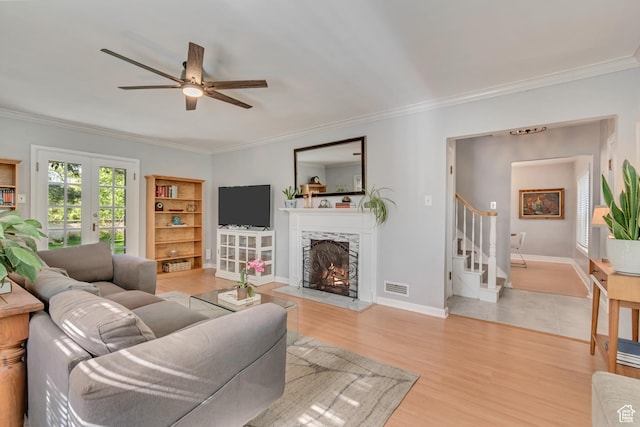 living room featuring stairs, crown molding, ceiling fan, a lit fireplace, and baseboards
