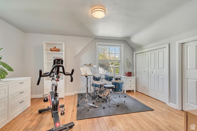workout room with light wood finished floors, baseboards, and vaulted ceiling