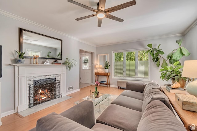 living area featuring a ceiling fan, a premium fireplace, crown molding, wood finished floors, and baseboards