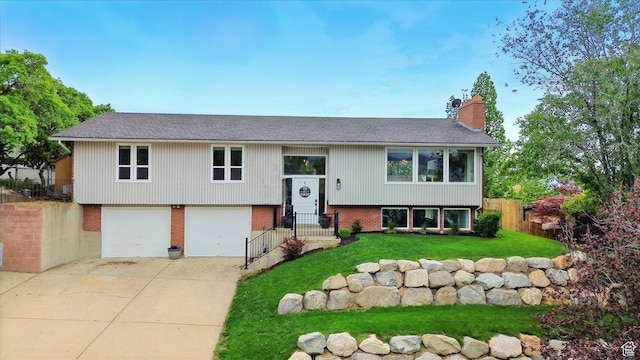 raised ranch featuring a chimney, brick siding, a garage, a shingled roof, and concrete driveway