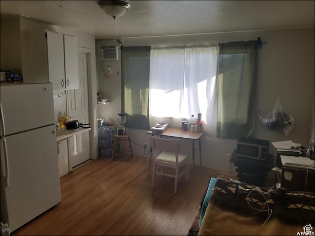 kitchen featuring freestanding refrigerator, wood finished floors, white cabinets, a wood stove, and a wall unit AC